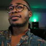 Brice Mansa in glasses and a patterned shirt, lit by green ambient light