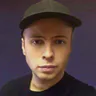 Michael Villari in a cap, photographed indoors under purple tinted light