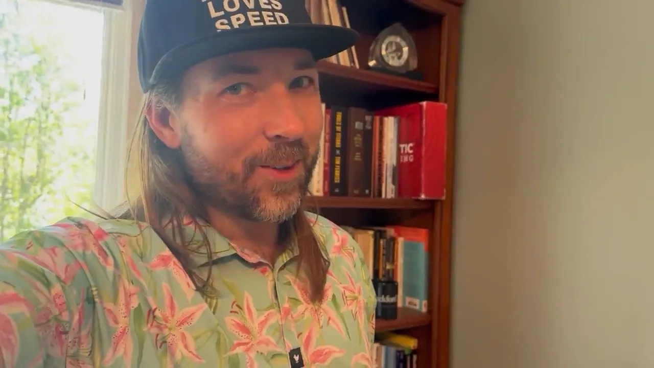 Quinton Hamp in a patterned shirt and cap, speaking to camera in his home office